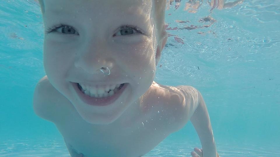 Närbild på ett glatt barn under vatten.