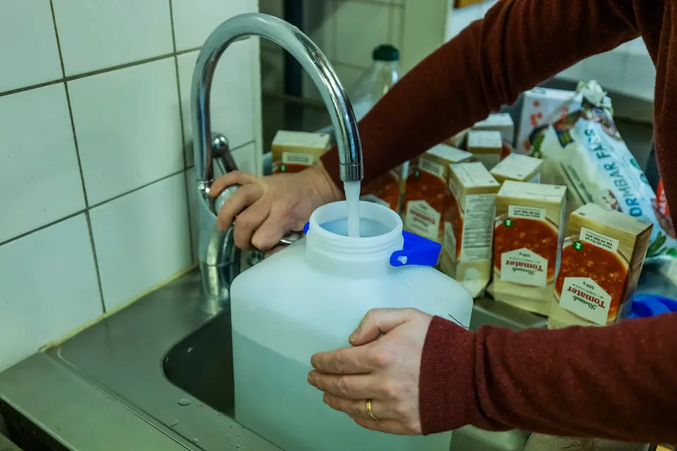 En bild på armarna på en person som håller på att fylla vatten i en plastdunk. Ena handen håller i dunken, den andra håller i vattenkranen.