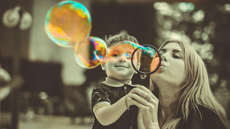 Kvinna och barn som blåser såpbubblor tillsammans.